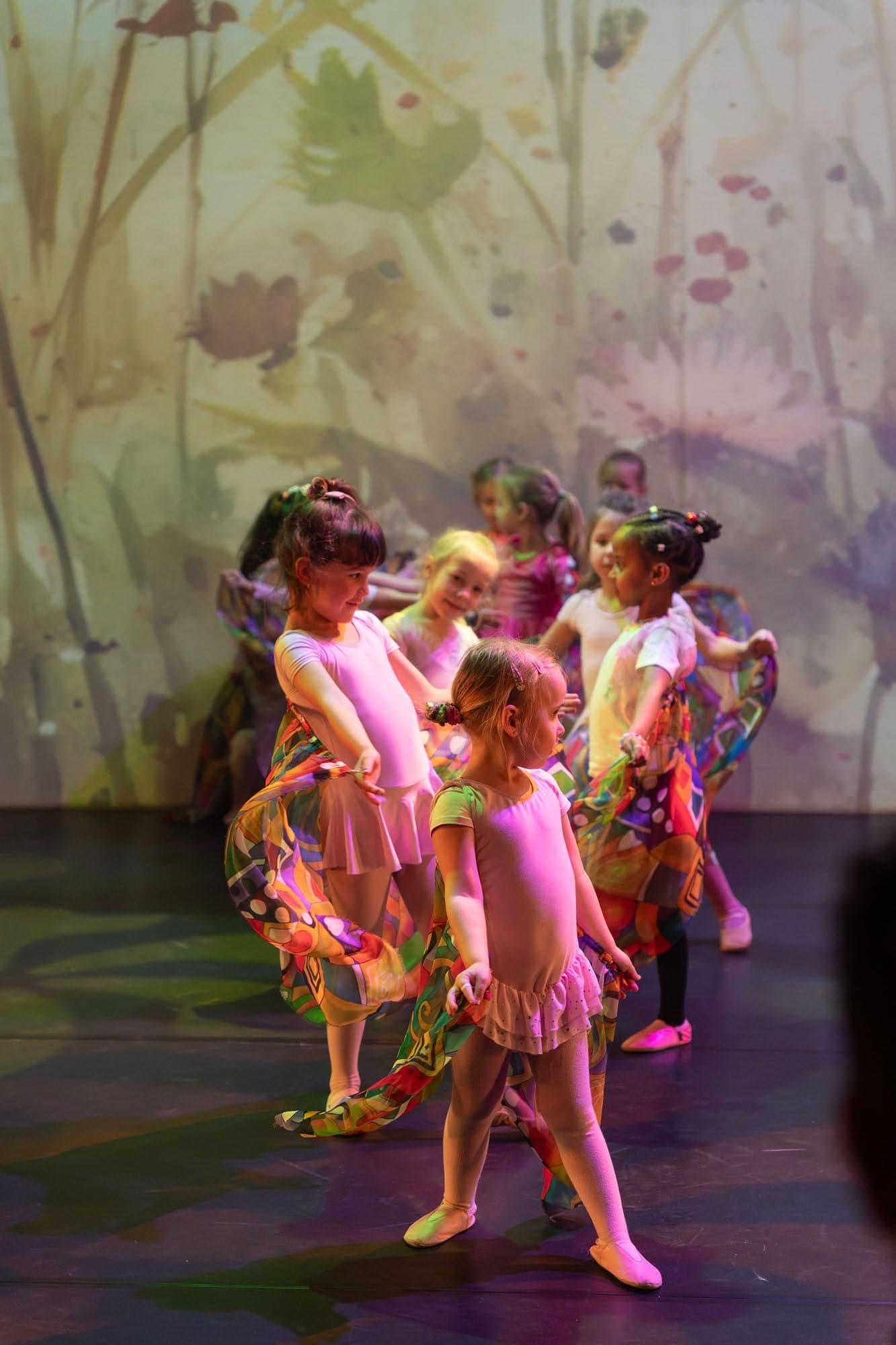 Kleuters in roze balletpakjes dansen samen op het podium voor een bloemendecor
